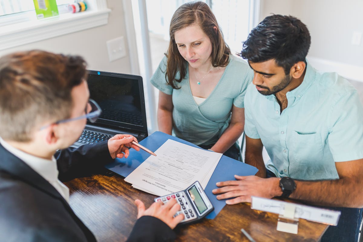 Property agent with calculator discussing pricing with a couple across an office table